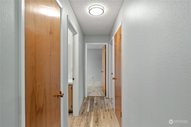 hallway featuring light hardwood / wood-style flooring and a textured ceiling