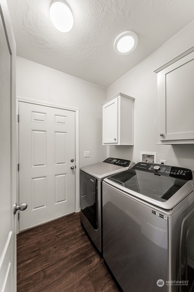 clothes washing area with cabinets, a textured ceiling, washing machine and dryer, and dark hardwood / wood-style flooring