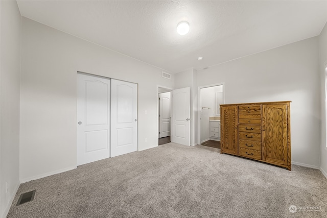 unfurnished bedroom with light carpet, a closet, and ensuite bathroom