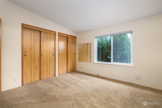 unfurnished bedroom with lofted ceiling, two closets, and carpet floors