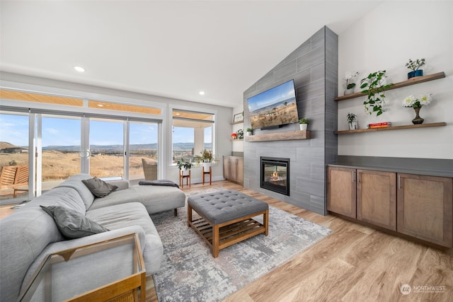 living room featuring lofted ceiling, light hardwood / wood-style flooring, and a tile fireplace