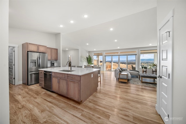 kitchen with sink, light hardwood / wood-style floors, stainless steel appliances, lofted ceiling, and a center island with sink