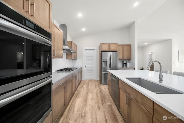 kitchen with sink, stainless steel appliances, wall chimney exhaust hood, lofted ceiling, and light hardwood / wood-style flooring