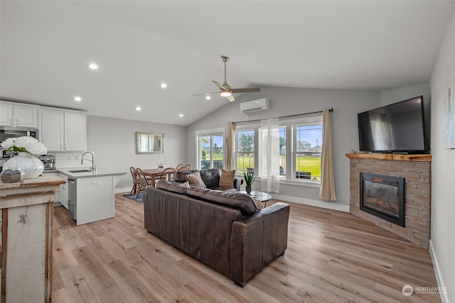 living room featuring a wall mounted AC, a stone fireplace, sink, vaulted ceiling, and light hardwood / wood-style floors