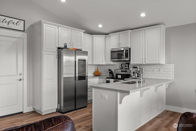 kitchen with decorative backsplash, a peninsula, white cabinetry, a sink, and appliances with stainless steel finishes