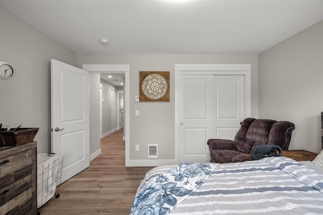 bedroom with baseboards, visible vents, wood finished floors, and a closet