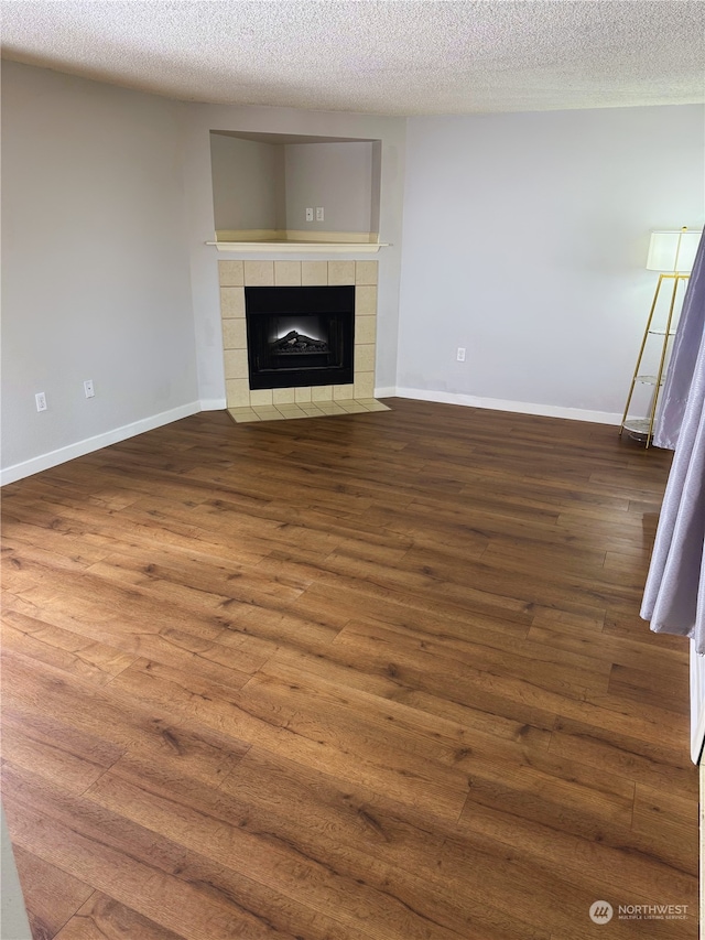 unfurnished living room featuring a tiled fireplace, dark wood-type flooring, and a textured ceiling