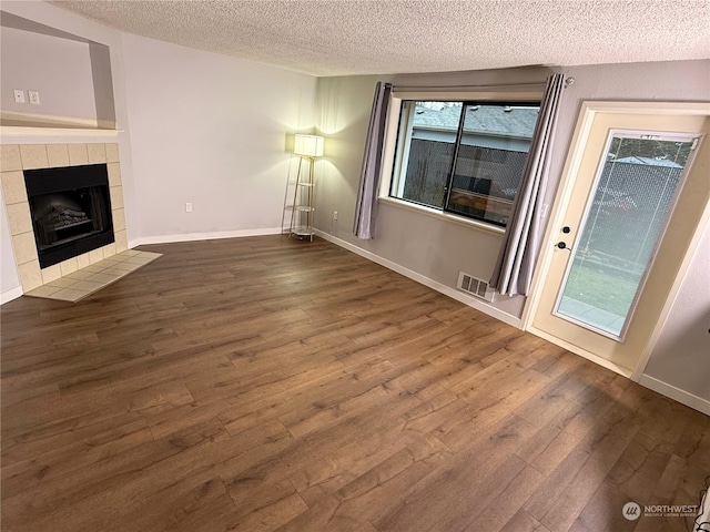 unfurnished living room featuring dark hardwood / wood-style flooring, a textured ceiling, and a tiled fireplace