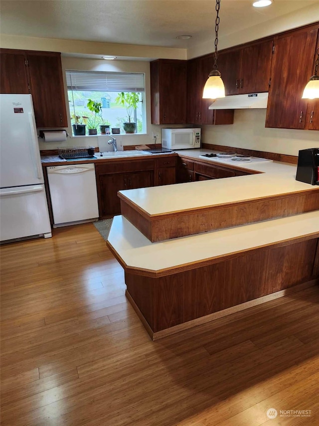 kitchen featuring pendant lighting, kitchen peninsula, light hardwood / wood-style flooring, and white appliances