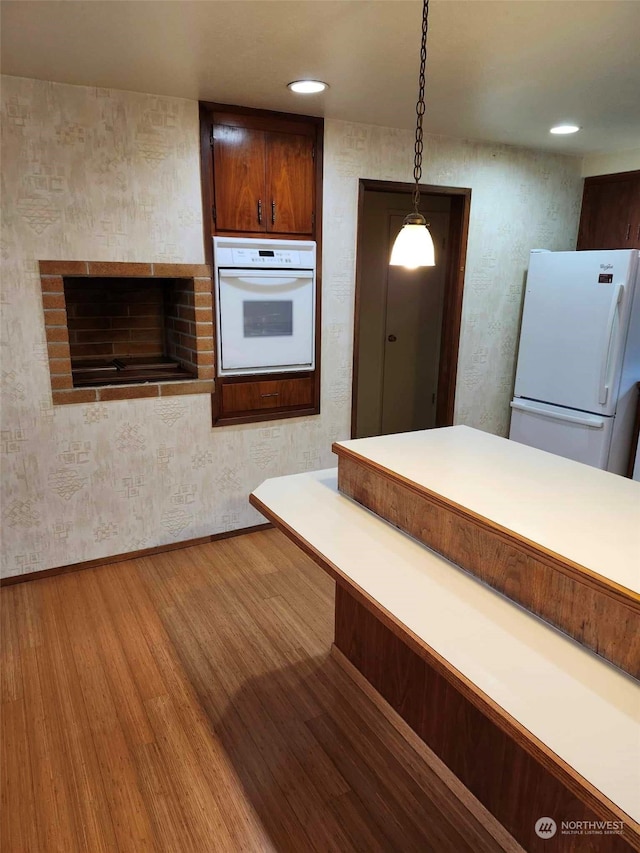 kitchen with pendant lighting, white appliances, and light wood-type flooring