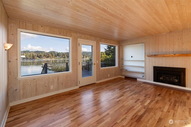 unfurnished living room featuring wood ceiling, hardwood / wood-style floors, built in shelves, wooden walls, and a water view