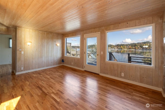 empty room with a water view, wood ceiling, wood walls, and light wood-type flooring