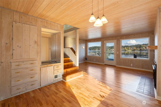 unfurnished living room with wooden walls, a notable chandelier, and light hardwood / wood-style floors