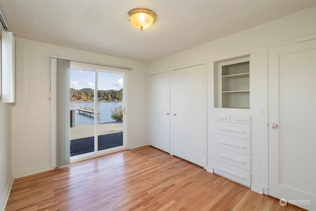 unfurnished bedroom featuring light hardwood / wood-style floors, access to outside, a closet, and a water view