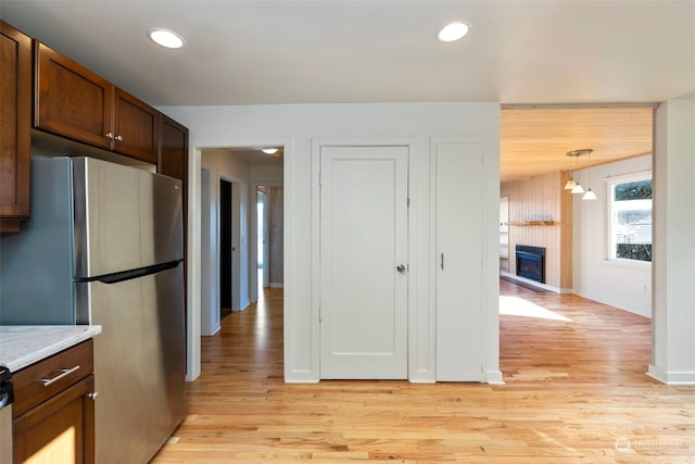 kitchen with light stone countertops, stainless steel refrigerator, light hardwood / wood-style flooring, and pendant lighting