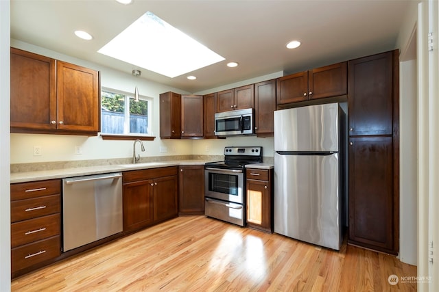 kitchen with appliances with stainless steel finishes, light hardwood / wood-style flooring, sink, and a skylight