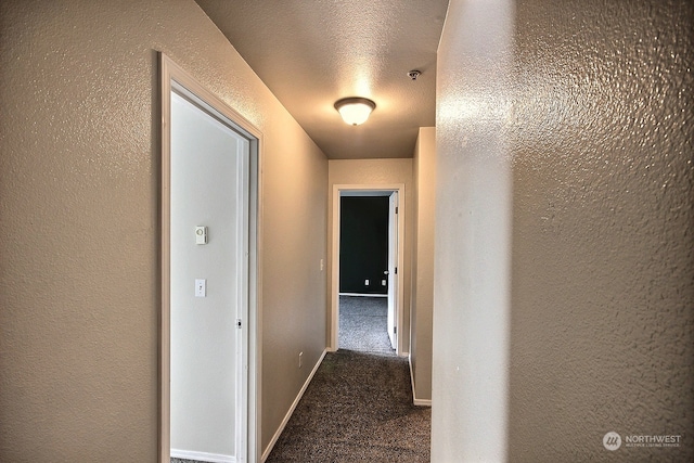 corridor featuring a textured ceiling and dark carpet