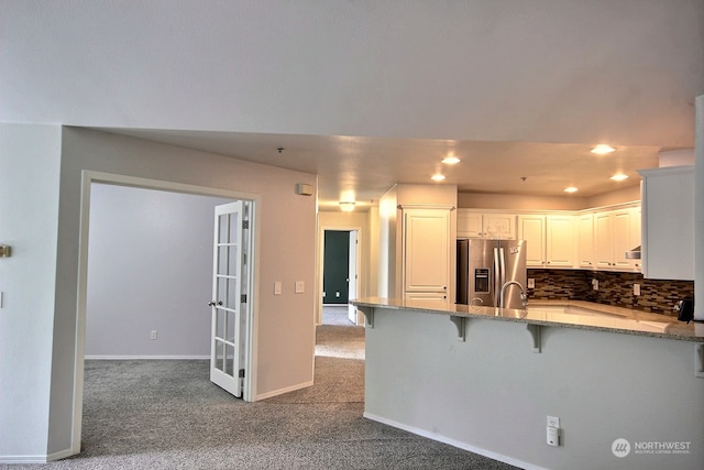 kitchen with kitchen peninsula, stainless steel fridge, a kitchen bar, white cabinetry, and tasteful backsplash