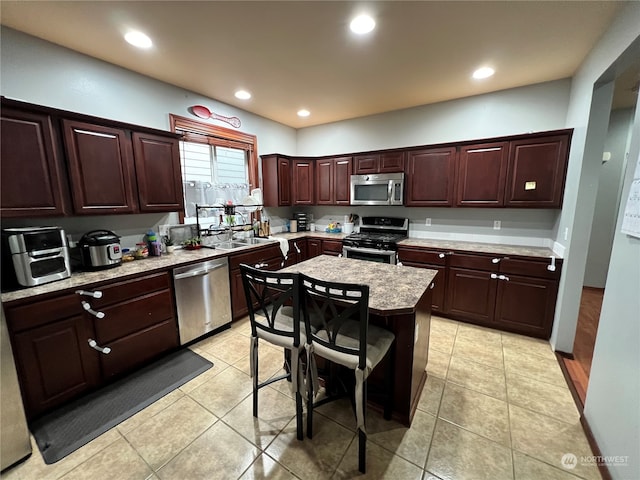 kitchen featuring appliances with stainless steel finishes, light tile patterned flooring, a kitchen island, and a kitchen breakfast bar