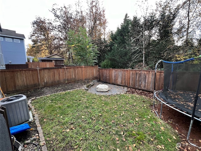 view of yard with an outdoor fire pit, a trampoline, and central AC unit