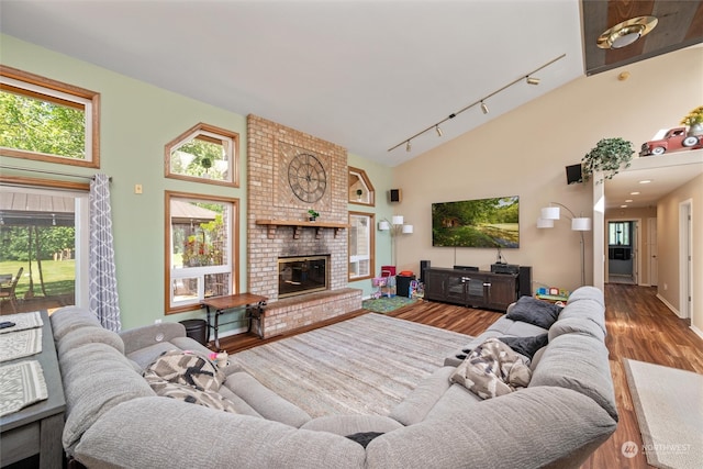 living room with high vaulted ceiling, track lighting, wood-type flooring, and a brick fireplace