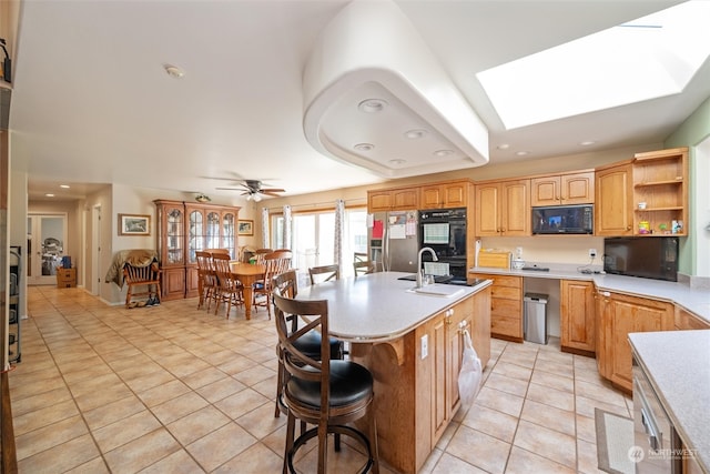 kitchen featuring black appliances, sink, a skylight, ceiling fan, and a center island with sink