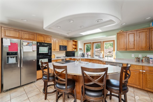 kitchen with a raised ceiling, black appliances, a kitchen bar, and a center island with sink