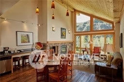 dining area with a stone fireplace, high vaulted ceiling, and dark wood-type flooring