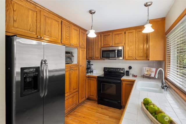 kitchen featuring appliances with stainless steel finishes, sink, hanging light fixtures, tile counters, and light hardwood / wood-style flooring