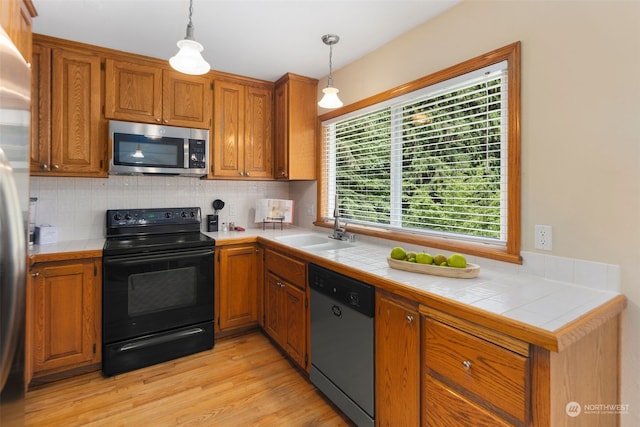 kitchen with appliances with stainless steel finishes, tile countertops, decorative light fixtures, and light hardwood / wood-style flooring