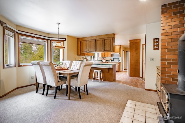 dining room featuring a wood stove, light colored carpet, and baseboards