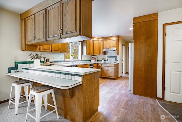 kitchen featuring a breakfast bar area, light countertops, brown cabinetry, light wood-style floors, and a peninsula