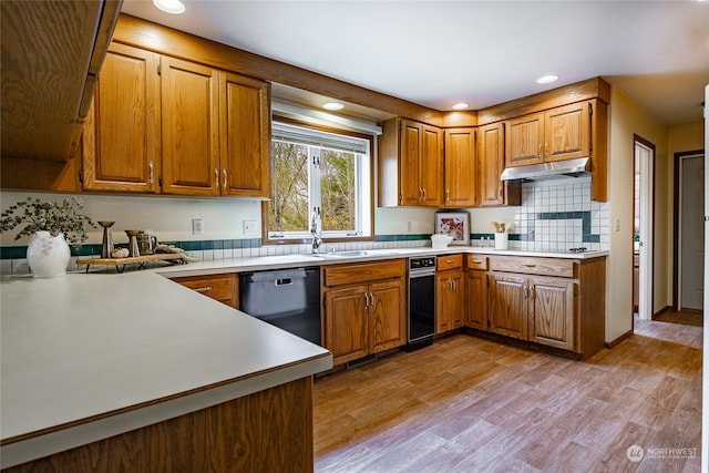 kitchen featuring under cabinet range hood, a sink, black dishwasher, light wood-type flooring, and brown cabinets