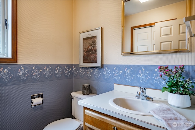 half bathroom with toilet, wallpapered walls, and vanity