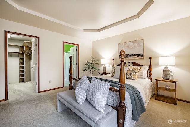 bedroom featuring a closet, a raised ceiling, light colored carpet, a spacious closet, and baseboards