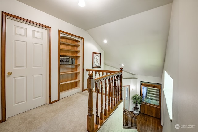 hallway with built in features, carpet, vaulted ceiling, and an upstairs landing