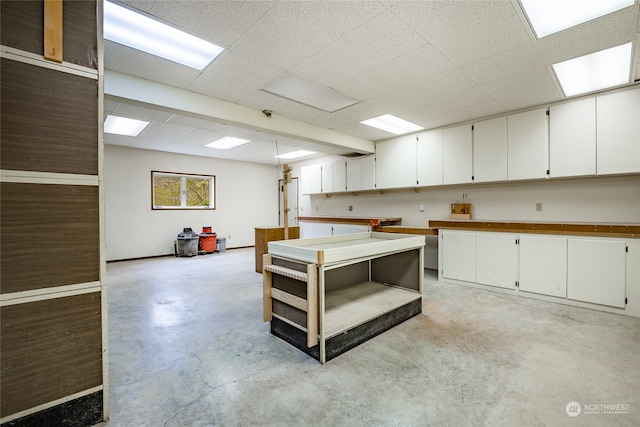 kitchen featuring a paneled ceiling, concrete floors, white cabinetry, and baseboards