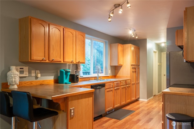 kitchen featuring kitchen peninsula, appliances with stainless steel finishes, a breakfast bar, light hardwood / wood-style flooring, and sink