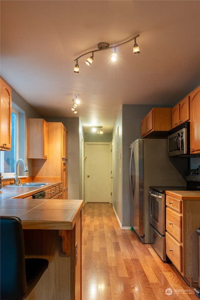 kitchen with appliances with stainless steel finishes, sink, tile countertops, rail lighting, and light hardwood / wood-style flooring