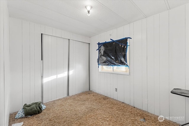 unfurnished bedroom with a closet, wood walls, and carpet flooring