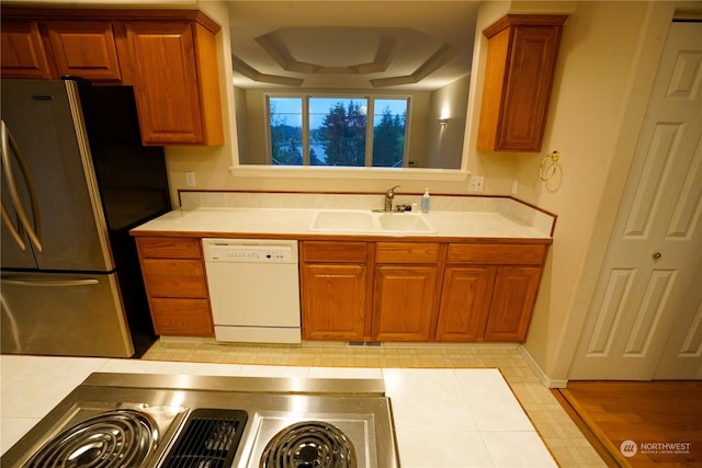 kitchen with dishwasher, a tray ceiling, sink, light wood-type flooring, and stainless steel refrigerator