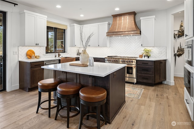 kitchen with appliances with stainless steel finishes, a kitchen breakfast bar, custom range hood, sink, and a center island