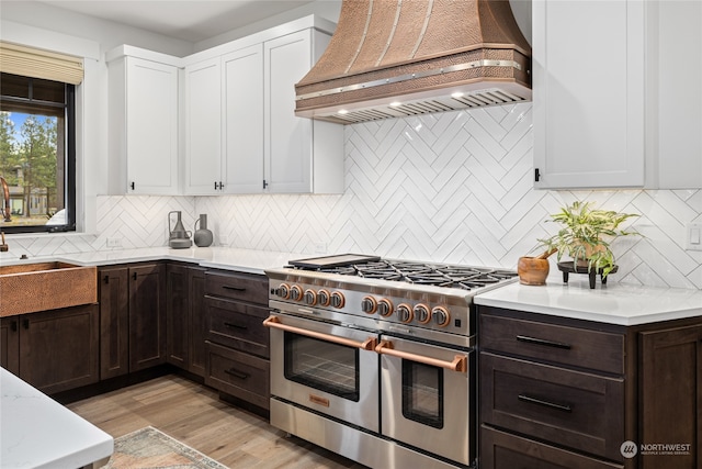 kitchen with range with two ovens, light hardwood / wood-style flooring, dark brown cabinetry, custom range hood, and white cabinetry