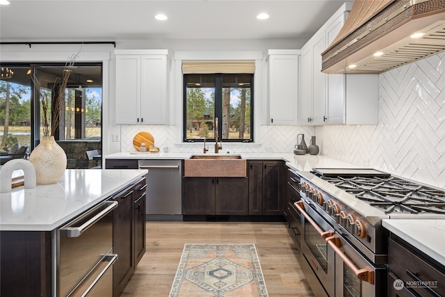 kitchen featuring custom exhaust hood, white cabinets, sink, light hardwood / wood-style flooring, and stainless steel appliances