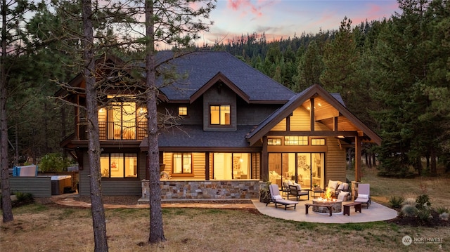 back house at dusk featuring an outdoor hangout area, a balcony, a patio area, and a lawn