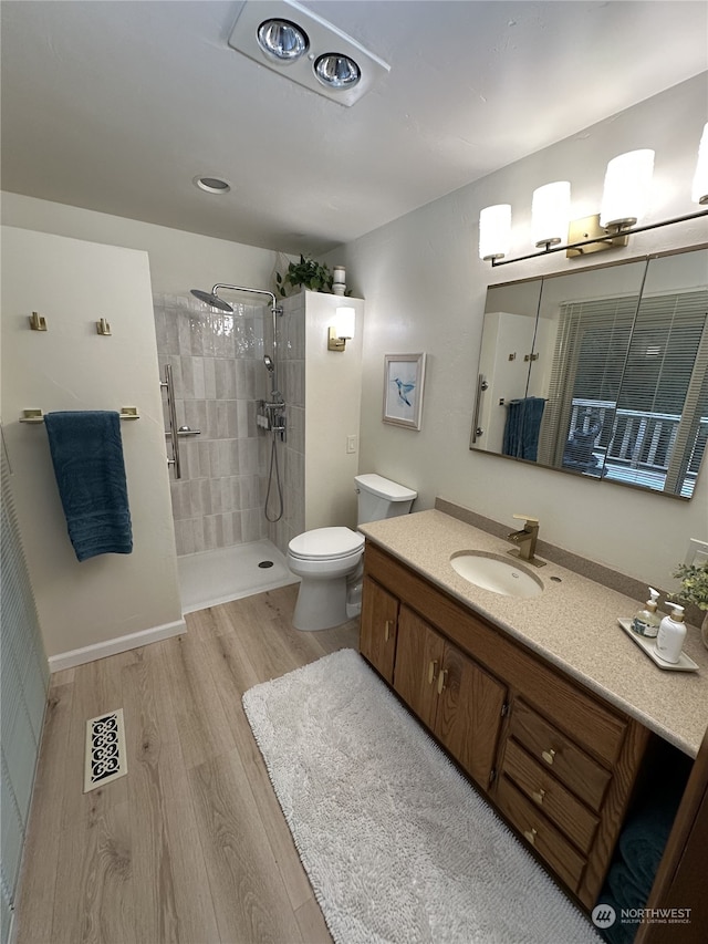 bathroom featuring vanity, hardwood / wood-style flooring, toilet, and tiled shower