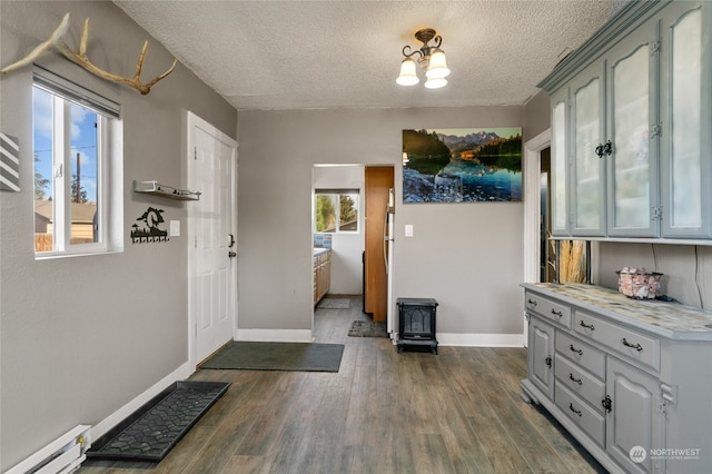 doorway with a wood stove, dark hardwood / wood-style floors, a textured ceiling, and a baseboard heating unit