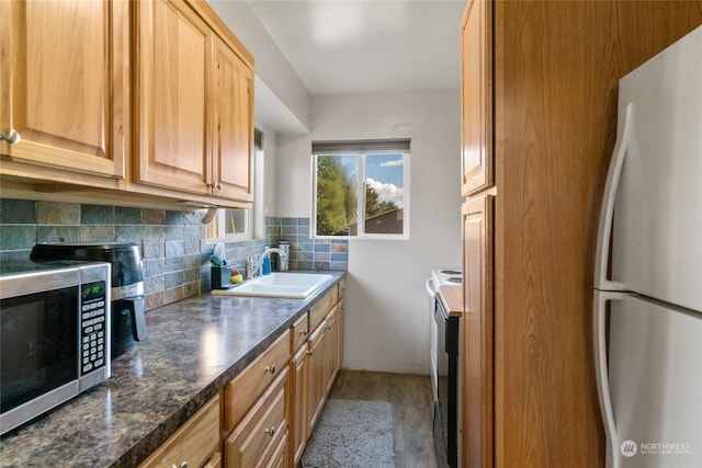 kitchen with stainless steel appliances, dark stone counters, sink, light hardwood / wood-style floors, and tasteful backsplash