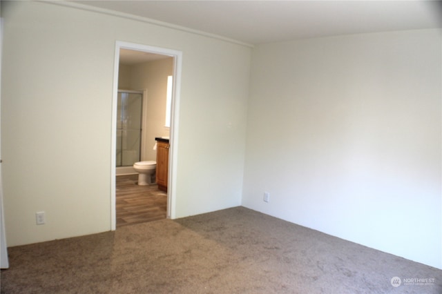 unfurnished bedroom featuring dark carpet and ensuite bath