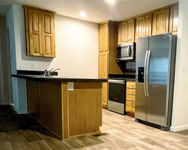 kitchen featuring kitchen peninsula, appliances with stainless steel finishes, sink, and light wood-type flooring